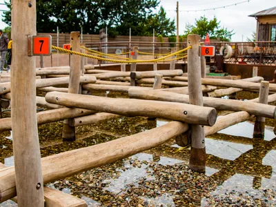 Miteinander verbundene Holzstäbe ragen aus dem Wasser-Stein-Boden. Die Stäbe sind mit roten Ziffern nummeriert und mit gelben Seilen verbunden.